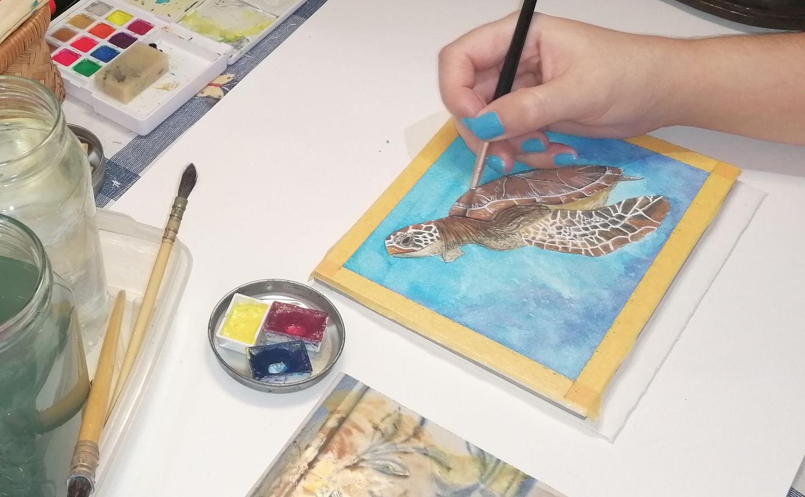 Photo of the Artist Eloma Arts painting a Green Sea Turtle with watercolor